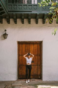 a woman standing in front of a door with her hands on her head and arms behind her head