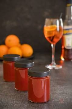 three glass jars filled with liquid next to oranges and a bottle of wine on a table