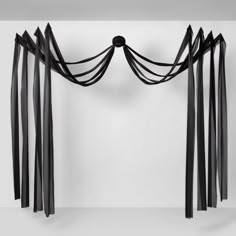 an abstract sculpture with black ribbons hanging from it's sides and on the wall