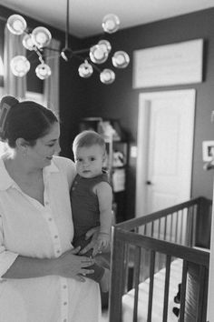 a black and white photo of a woman holding a baby in her arms while standing next to a crib