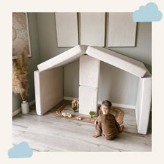 a toddler playing with a play house made out of cardboard boxes on the floor