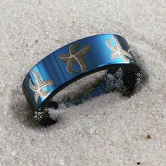 a close up of a bracelet on the ground with sand around it and sea shells