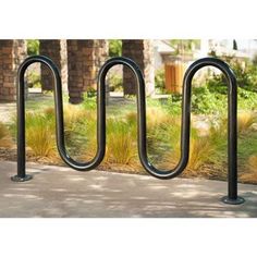 three black metal bike racks on the side of a sidewalk next to grass and trees