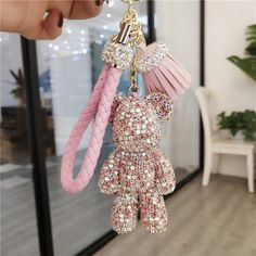 a pink keychain hanging from the side of a glass door with a teddy bear charm attached to it