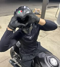 a man sitting on top of a motorcycle wearing black gloves and holding his hands to his face