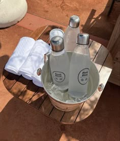 two bottles of water are sitting in an ice bucket on a wooden table with towels