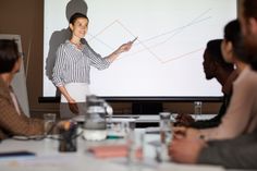 a group of people sitting around a table in front of a projector screen with a man giving a presentation