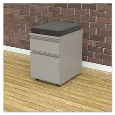 a gray filing cabinet sitting on top of a hard wood floor next to a brick wall