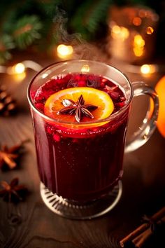 a glass mug filled with red liquid next to an orange slice and cinnamon on a table