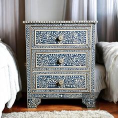 a blue and white chest of drawers sitting on top of a wooden floor next to a bed