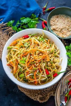 a white bowl filled with noodles and vegetables next to some silverware on a table