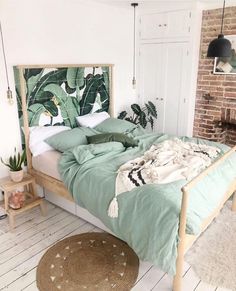 a bed with green sheets and blankets in a room next to a brick wall, potted plant on the floor