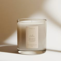 a candle with a label on it sitting in front of a white wall and shadow