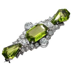 A spectacular early twentieth century brooch centered around an emerald cut peridot, surrounded by diamonds, and finished on either side with shield cut peridot. The central stone weighs approximately 10.5ct, and the combined weight of the two shield cut peridot is approximately 7.5ct. The 4 diamonds set along the 4 sides of the center peridot weigh approximately 2.5ct. total weight. The diamonds accenting the geometric design of the brooch weigh a total of approximately 1.66ct. Overall color of the diamonds is J color, and overall clarity is VS2-SI2. Measuring 2 1/4 inches long, by 7/8 inch wide, it is noticeable, while being very tasteful. Gross weight 14 grams. Peridot Brooch, 1920s Jewelry, Art Deco 1920s, Antique Vintage Jewelry, Art Deco Period, August Birth Stone, Antique Art Deco, Antique Art, Emerald Cut