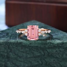 a pink tourmaline ring sitting on top of a green marble block with diamonds around it