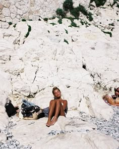 two women are sitting on the rocks in the water and one is wearing a bathing suit