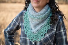 a woman standing in a field wearing a green scarf and plaid shirt with her hands on her hips