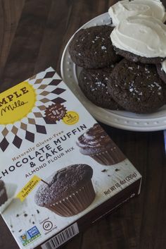 a box of chocolate muffins next to a plate of cupcakes