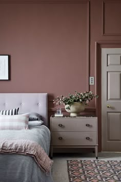 a bedroom with a bed, dresser and pink wall paint in the corner is a vase with flowers on it