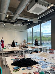 people are standing in an open room with tables and posters on the walls, looking out over water