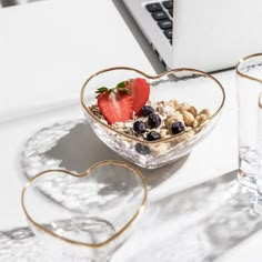 a heart shaped bowl filled with cereal and fruit on top of a table next to two glasses