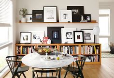 a dining room table and chairs with pictures on the wall above it, along with bookshelves