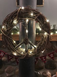 a peace sign made out of branches with lights around it on a pole in front of a fireplace