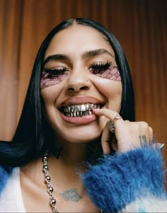 a woman with black hair and purple eyeliners smiles while holding her finger to her mouth