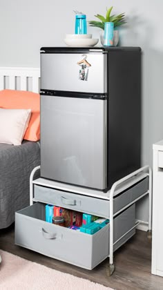 a silver refrigerator freezer sitting on top of a metal drawer next to a bed