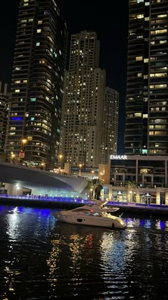 boats are docked in the water near tall buildings at night with bright lights on them