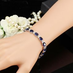 This stunning bracelet features 17 oval shaped Austrian Crystals in brilliant blue colors. Each stone is accented with two smaller crystals on each side creating the perfect contrast to the brightly colored stones. Deep, rich blue stones paired with vibrant, light catching cz diamonds create a luxurious piece for any occasion. Clasp closure for added security. Fit for royalty and a beauty for any occasion. Material: 14K White Gold Plated. Stones: 7mm x 5mm Austrian Cystal and 1.5 mm CZ Stones. S Blue Crystal Bracelets For Formal Occasions, Elegant Blue Crystal Bracelet With Sparkling Stones, Elegant Blue Bracelets With Sparkling Stones, Elegant Sapphire Crystal Bracelets, Elegant Blue Cubic Zirconia Crystal Bracelet, Blue Oval Bracelet As A Gift, Blue Oval Bracelet As Gift, Oval Blue Diamond Bracelets, Blue Gemstone Bracelet In Cubic Zirconia