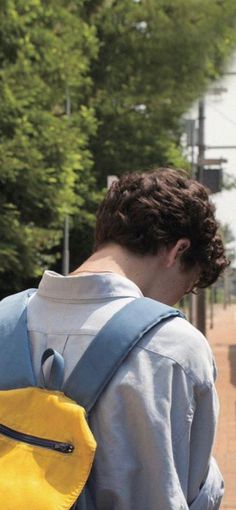 a young man with a yellow backpack on his back walking down the street in front of a bus