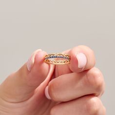 a woman's hand holding a gold ring with blue stones