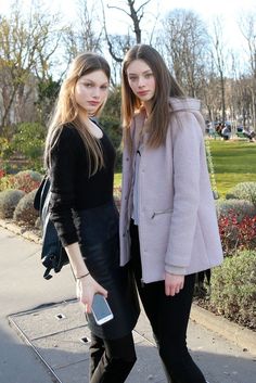 two young women standing next to each other on a sidewalk with trees in the background