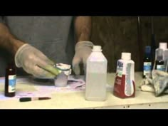 a person with gloves on is doing something in front of bottles and paintbrushes