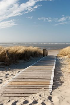 a wooden walkway leading to the beach with grass and sand in the background on a sunny day