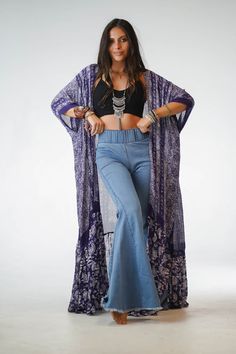 a woman is posing with her hands on her hips and wearing bell bottoms, an open - front kimono, and beaded necklaces