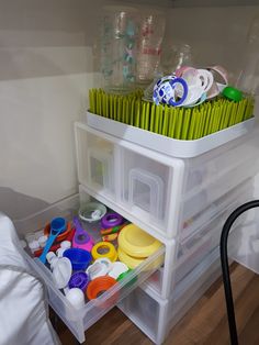 plastic storage bins filled with craft supplies on top of a wooden floor next to a bed