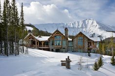 a large house in the middle of a snow covered field with mountains in the background