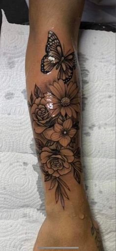 a woman's foot with flowers and a butterfly tattoo on the side of her leg