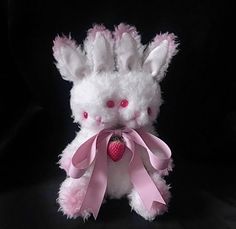 a white stuffed animal with pink ribbon around it's neck and ears, holding a strawberry in its mouth