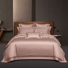 a bed with pink comforter and pillows in a room next to a night stand