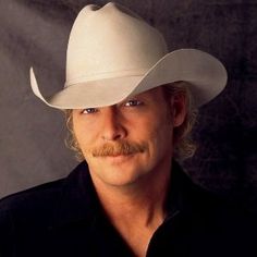 a man wearing a white cowboy hat and black shirt posing for a photo in front of a gray background