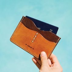 a hand holding two credit cards in a leather card case with stitching on the front