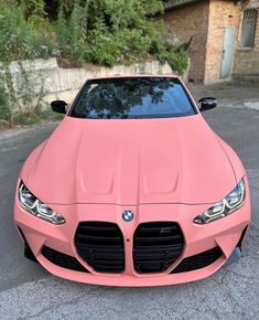 the front end of a pink sports car parked in a parking lot next to trees