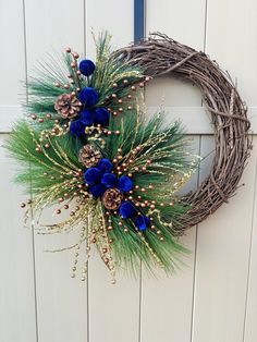 a wreath with blue flowers and pine cones is hanging on the wall next to a door