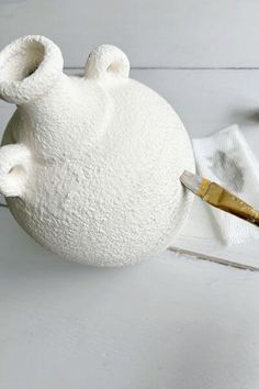 a white vase sitting on top of a table next to a brush and paper towel