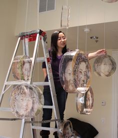 a woman is standing on a ladder and looking up at some glass plates hanging from the ceiling