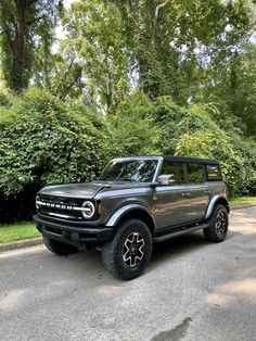 an suv is parked on the side of the road in front of some bushes and trees