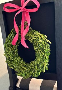 a green wreath with pink ribbon hanging on a black framed piece of art next to a roll of toilet paper